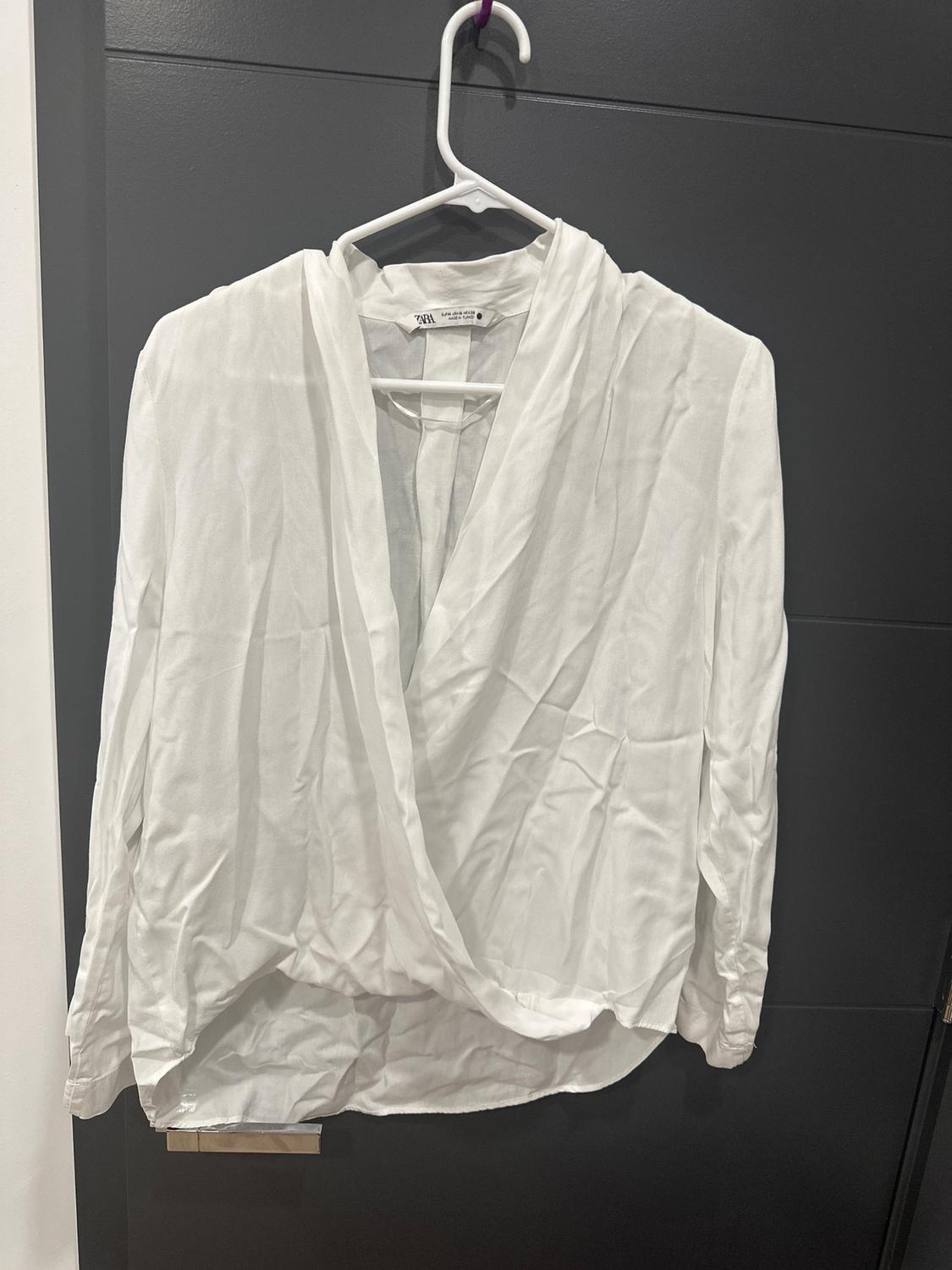 White long-sleeved shirt hanging on a white hanger over a dark door. Lightweight fabric with a crisscross design on the front.