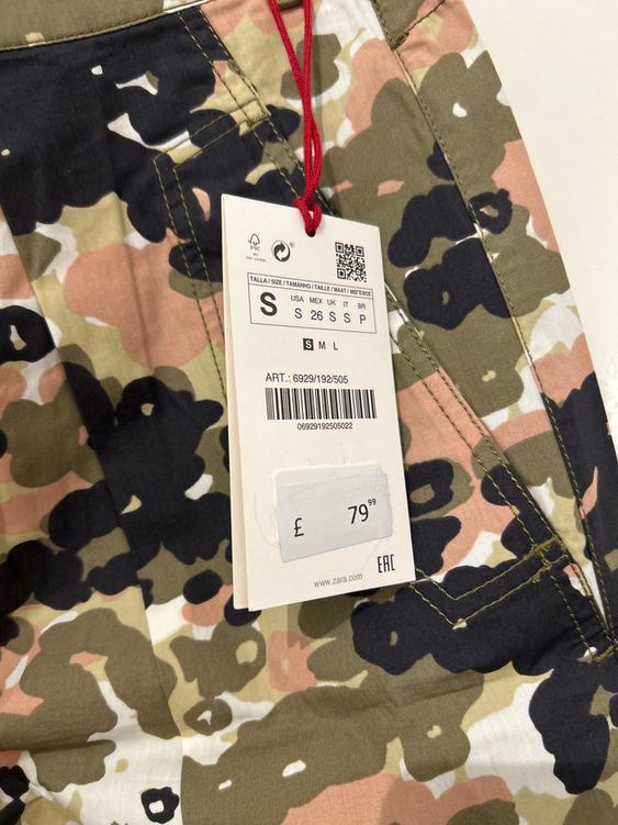 Trousers with camouflage print in green, black, and pink tones. Label with price £79.99 and size S. Item code: 6929/192/505.