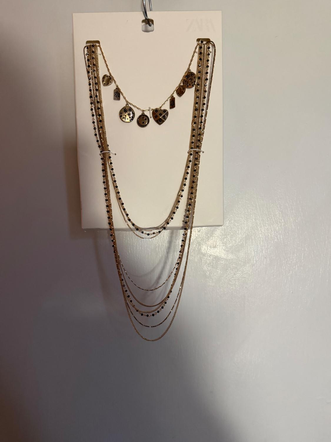 Gold necklace with multiple chains and heart and circle pendants, hanging on a white card.