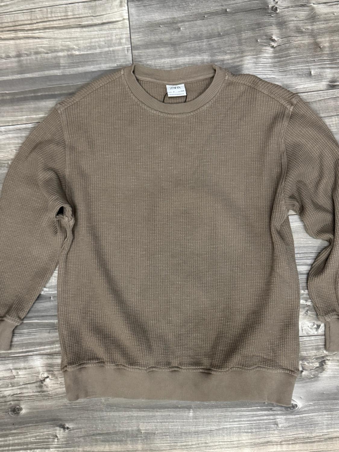 Brown long-sleeved sweatshirt with a textured finish against a wooden background. ZARA label visible at the neckline.