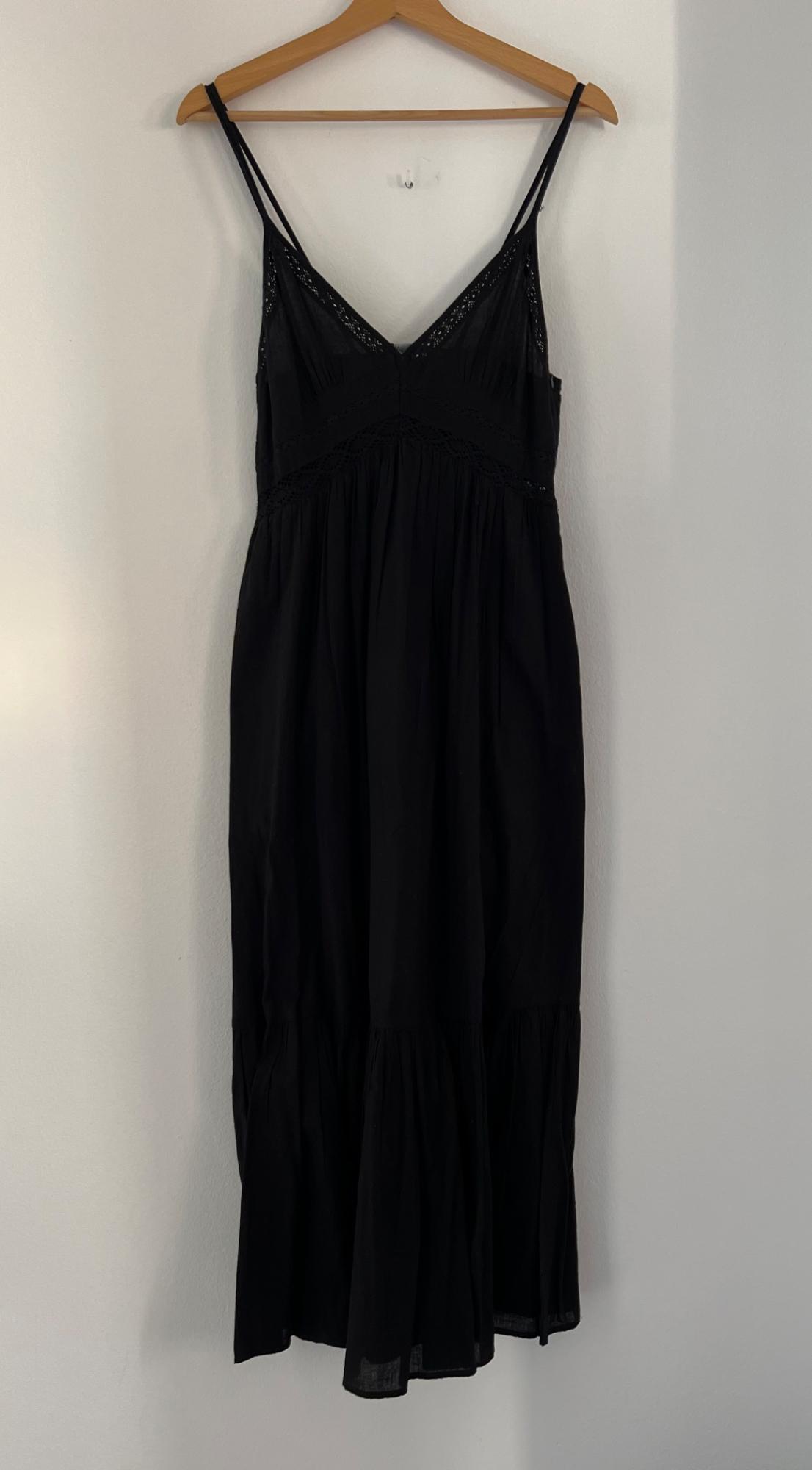 Black slip dress hanging on a wooden hanger. Lace detailing on the neckline and waist. White background.