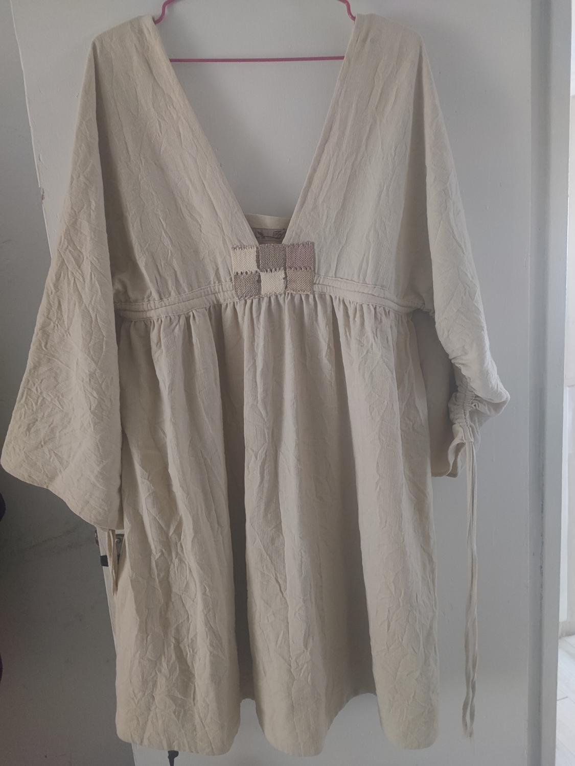 Creased beige fabric dress with a deep V-neckline and long sleeves, hanging on a pink hanger over a white door.
