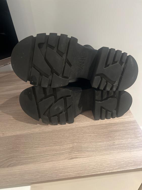 Black boot sole with a robust grip design, placed on a light wooden surface. Visible text: "ZARA".