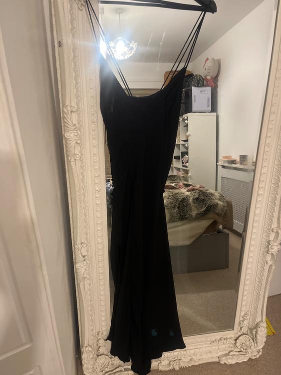 Black dress hanging on a white decorative mirror in a room. Reflection of a lamp and a bed with a faux fur blanket.