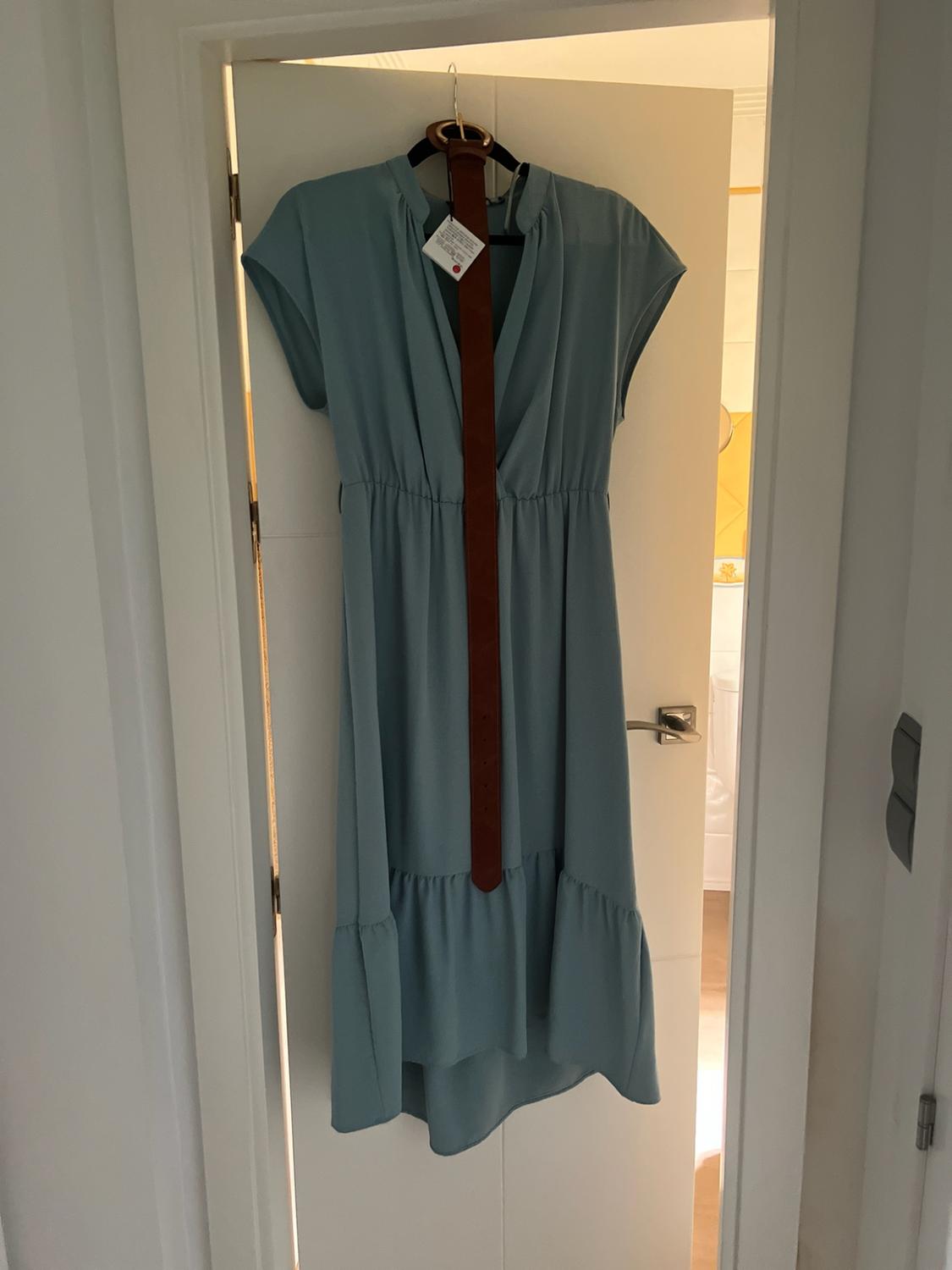 Light blue V-neck dress with a ruffled hem, hanging on a white door. A brown belt hangs over it. Casual style.
