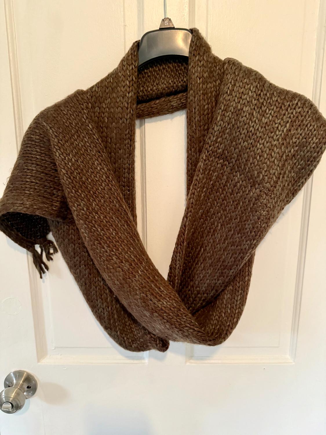Brown knitted scarf hanging on a black hanger with the letter "S", over a white door with a silver knob.