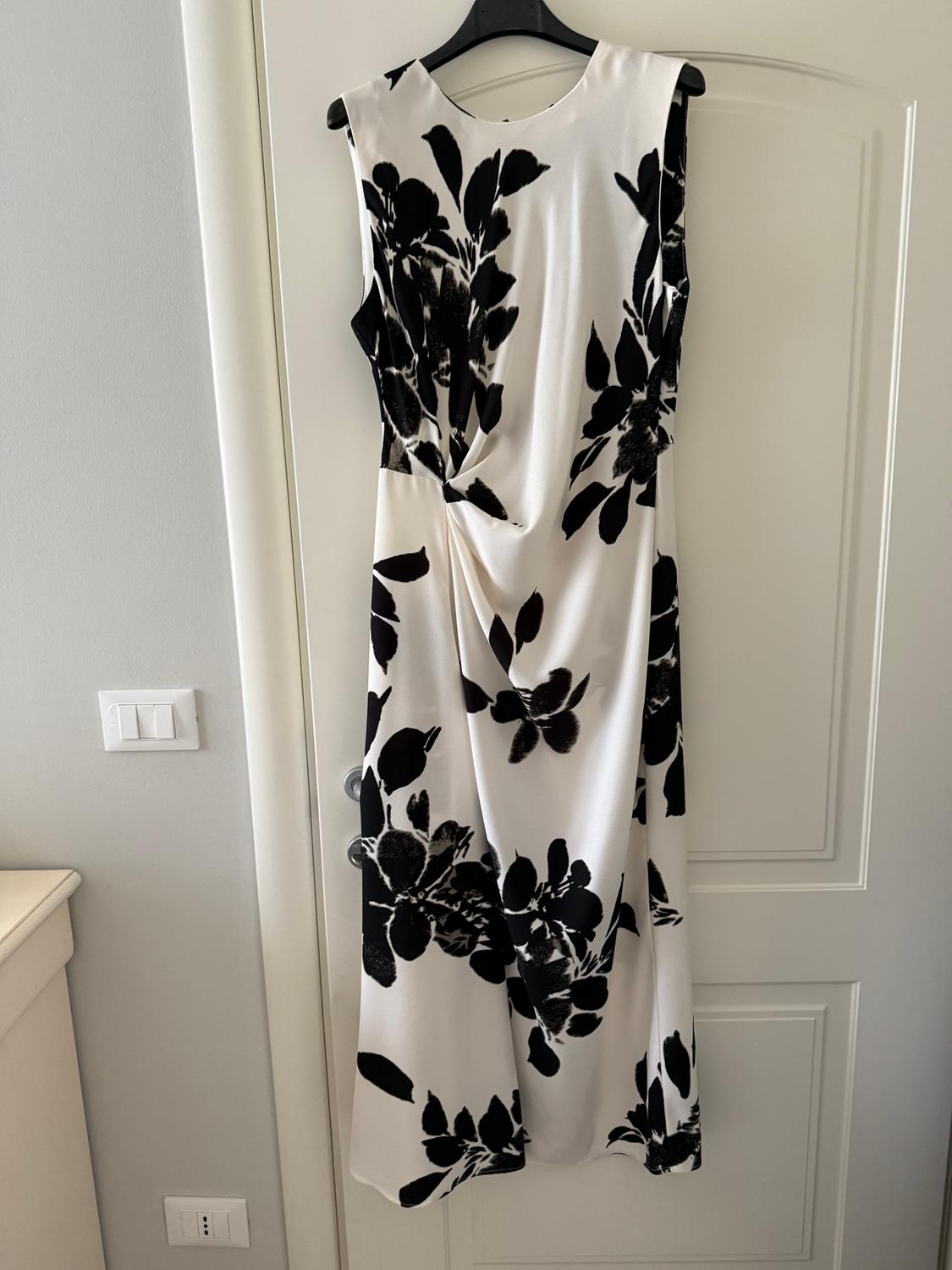 Sleeveless white dress with black floral print, hanging on a hanger over a white door.