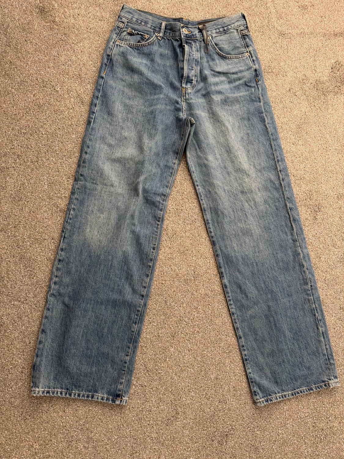 Blue straight-leg jeans with slight distressing, on a beige carpet.