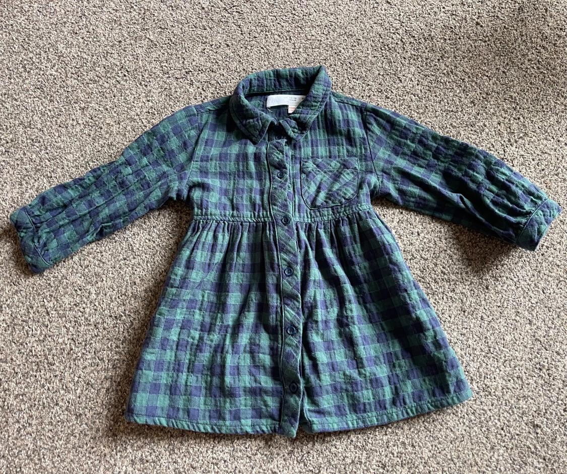 Girl's long-sleeved shirt with a green and blue checked pattern, on a beige rug.