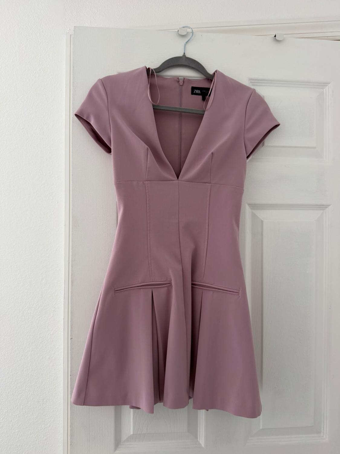 Pink short dress with a V-neck and short sleeves, hanging on a hanger over a white door.