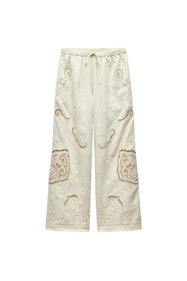 Front view of beige trousers with embroidery and an elasticated waistband.