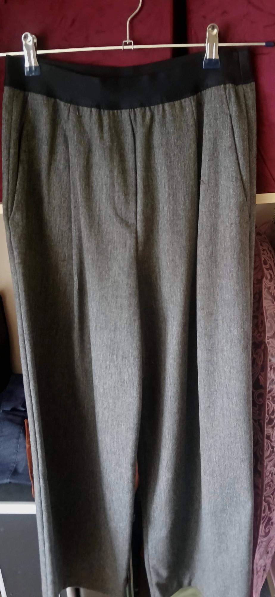 Grey fabric trousers hanging on a hanger with pegs, red fabric background and clothing details in the surroundings.