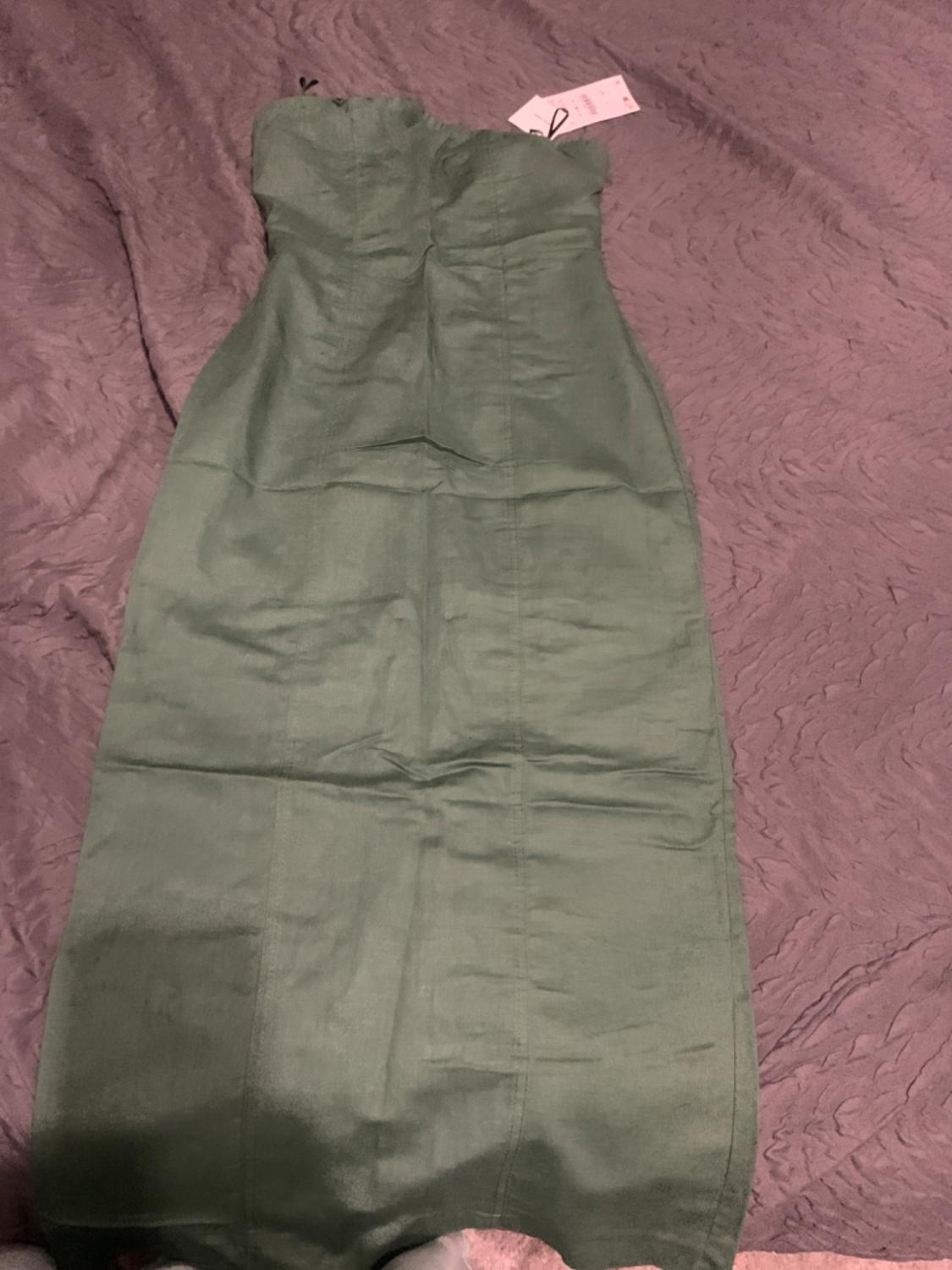 Strapless green dress on a textured grey bed. Label visible at the top of the dress.