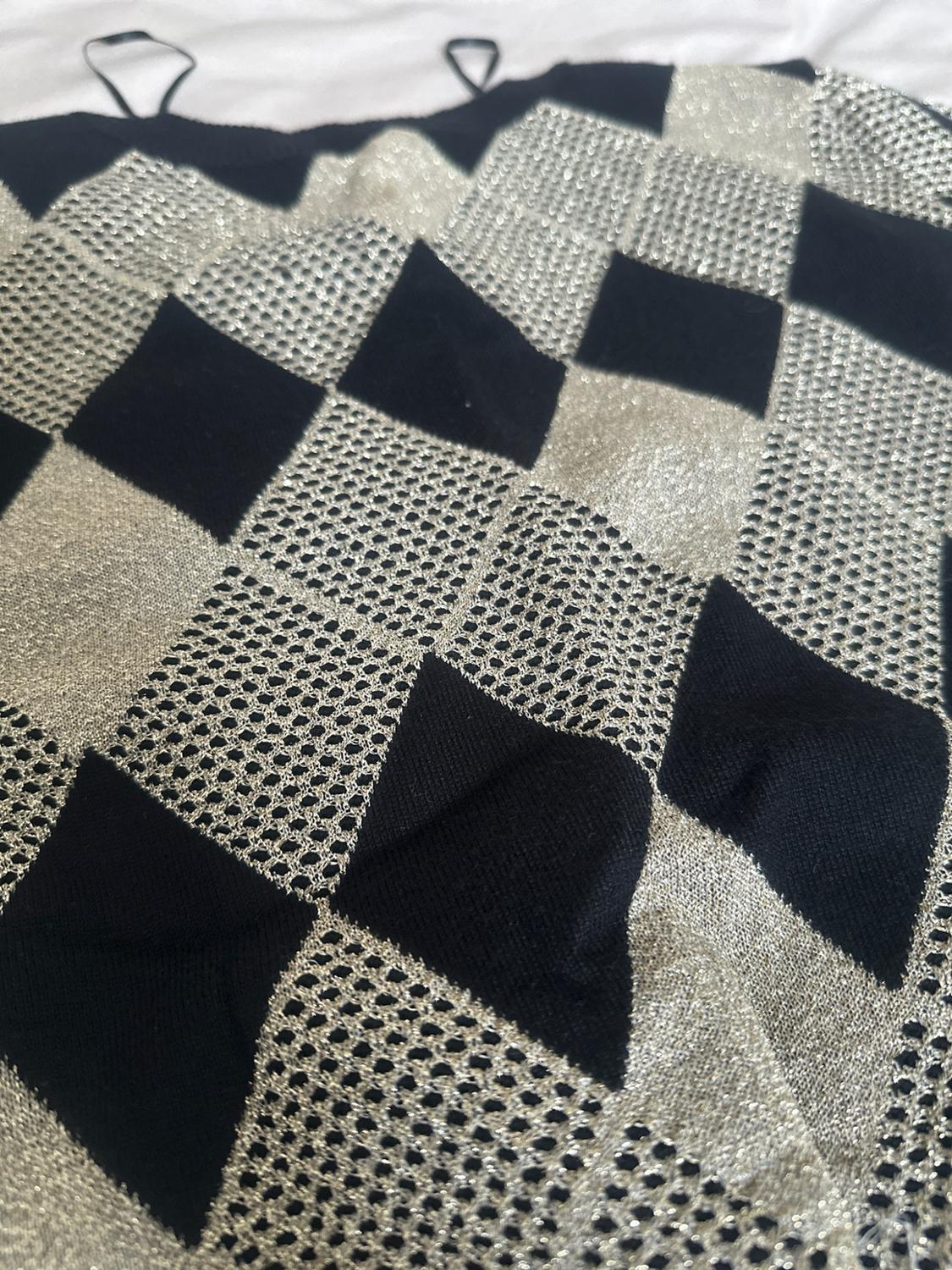 Close-up of a knitted garment with thin straps and a black argyle pattern with shiny metallic mesh, against a white background.