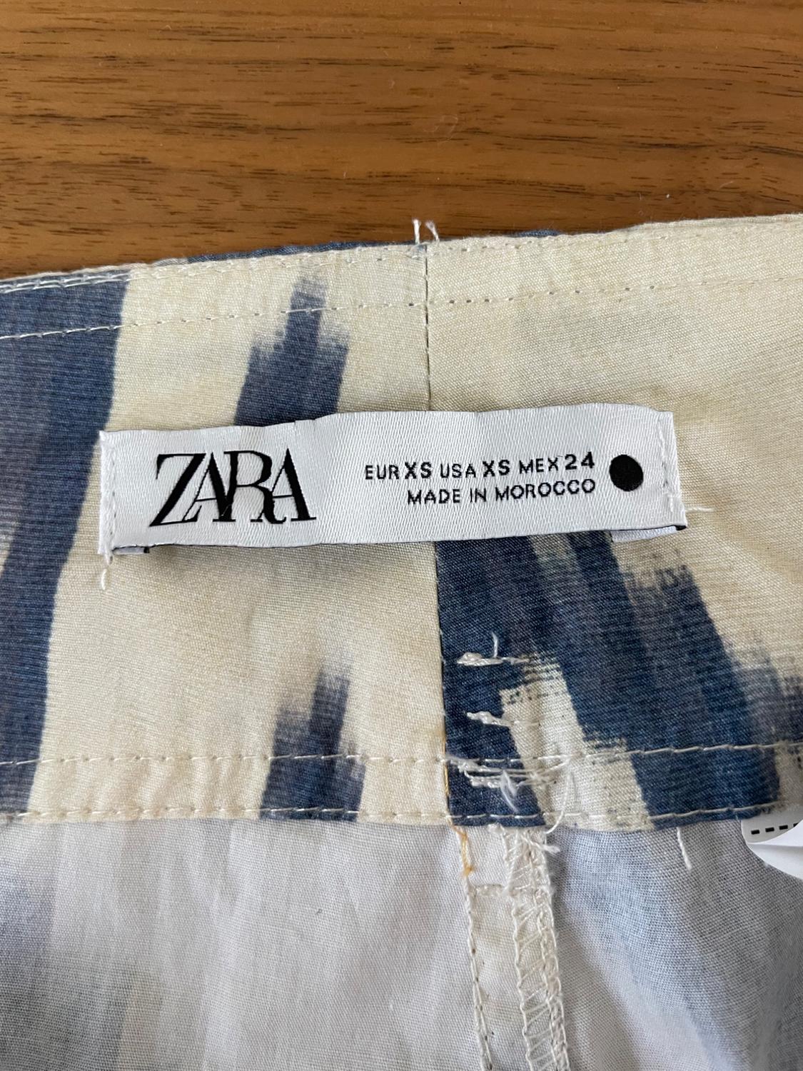 White label sewn onto a blue patterned fabric. Text: ZARA EUR XS USA XS MEX 24 MADE IN MOROCCO.