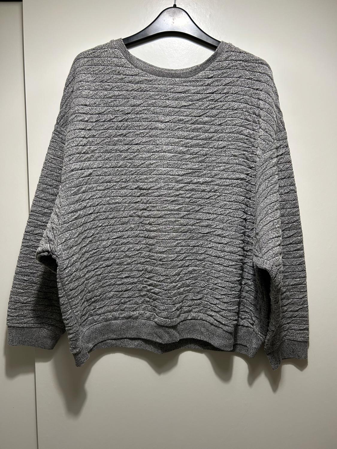 Textured grey jumper hanging on a black hanger against a white background.