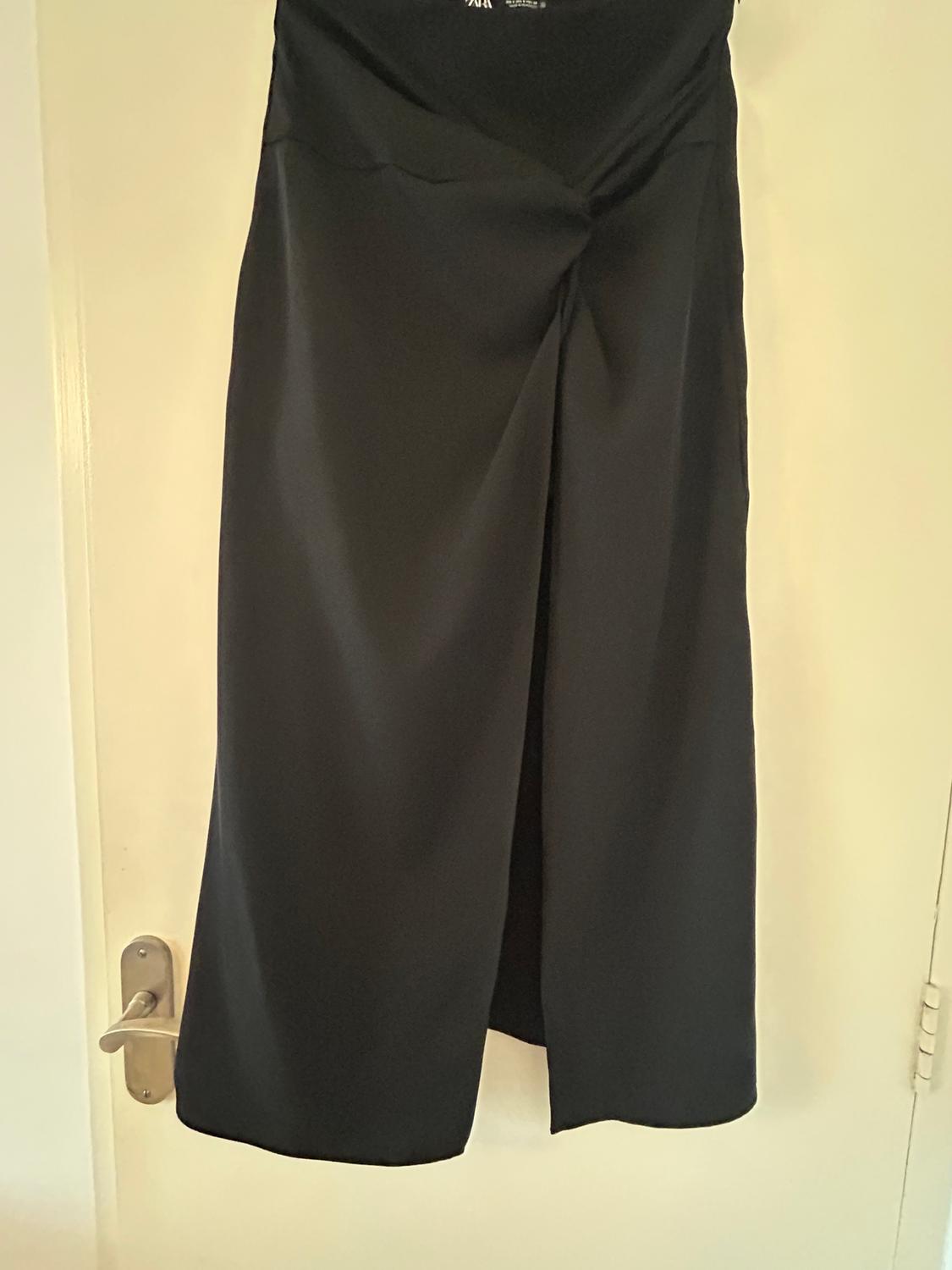 Black trousers hanging on a white door, with a wide-leg design and front pleat. Well-lit indoor setting.