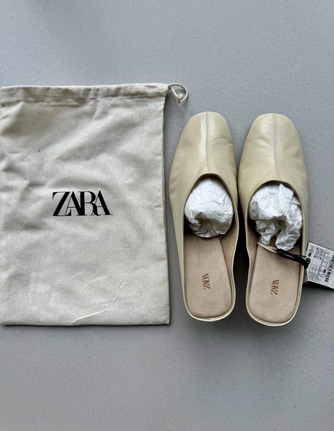 Beige backless shoes beside a fabric bag with the text ZARA on a light grey background.