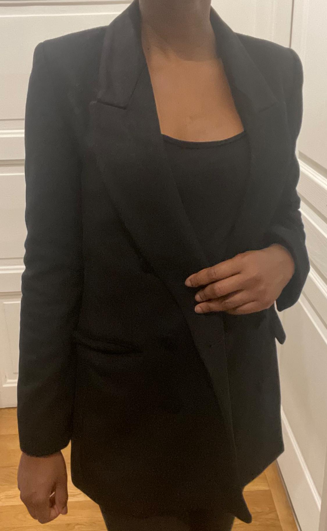 Model wearing a black blazer and matching t-shirt, indoors with a background of white doors and a wooden floor.