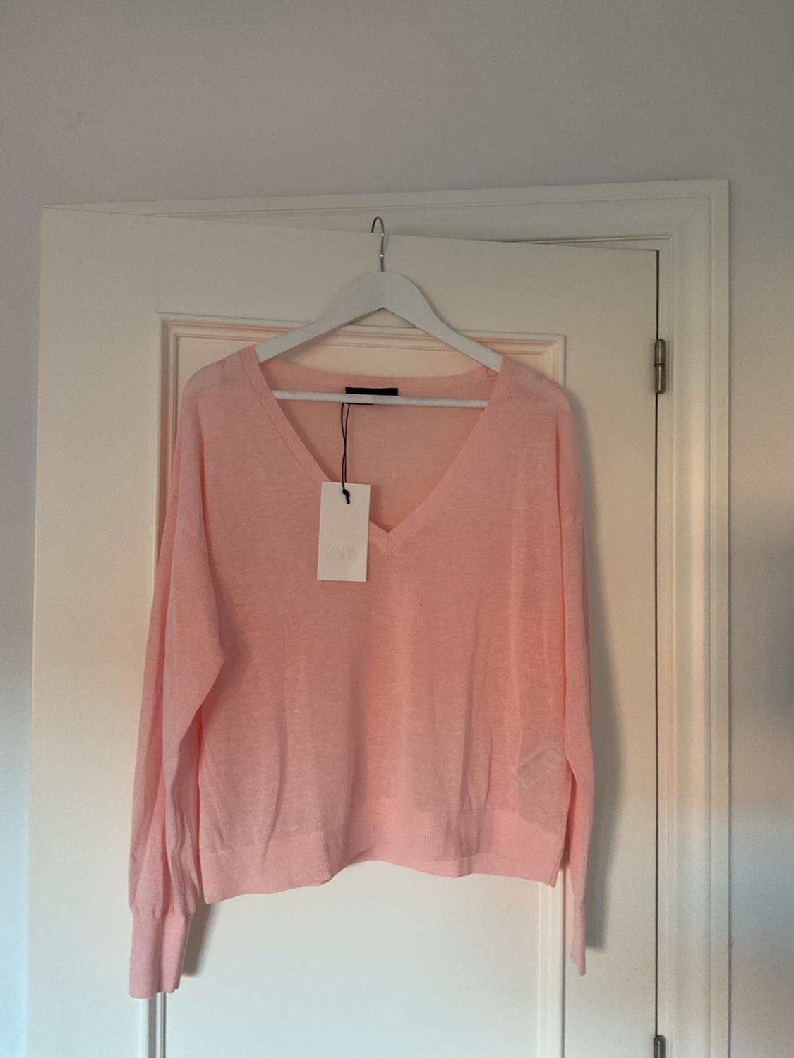 Light pink long-sleeved V-neck jumper hanging on a white hanger against a white door.