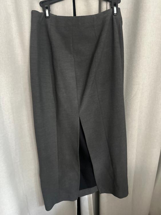 Long gray skirt with a front slit, hanging on a hanger against a beige curtain background.