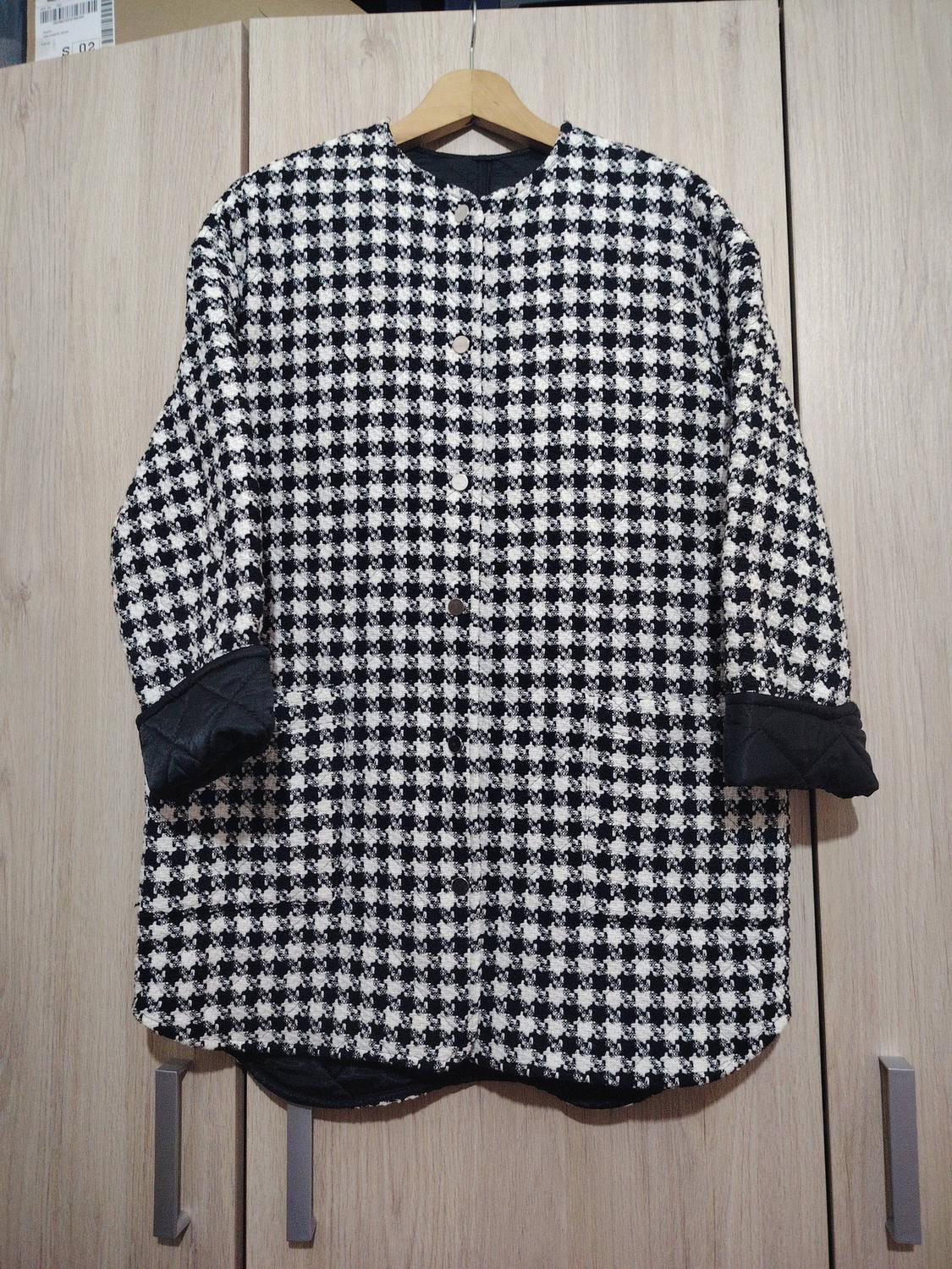 Black and white checked jacket hanging on a wooden hanger against a backdrop of light wood wardrobe doors.