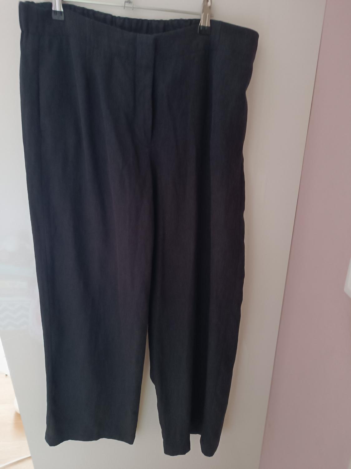 Black trousers hanging on a hanger over a white door. Fabric with a soft texture and a straight drape. Lit interior setting.