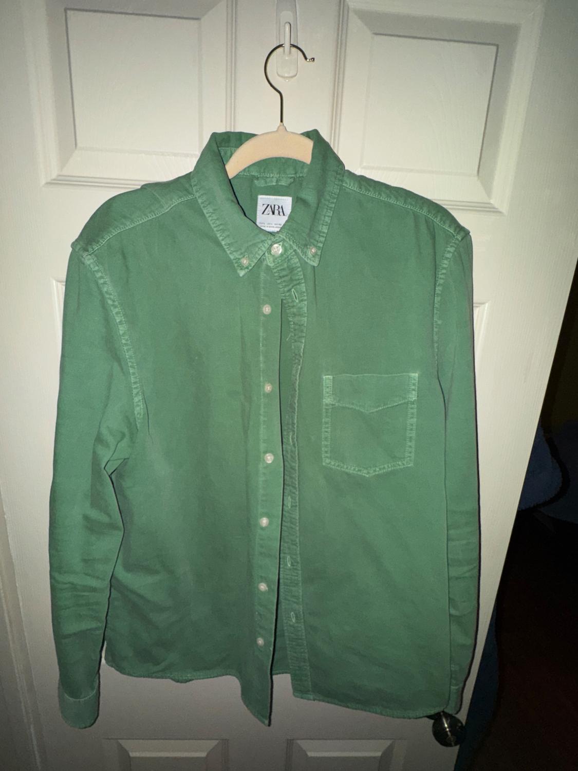 Green long-sleeved shirt hanging on a white door. Visible label with the text "ZARA".