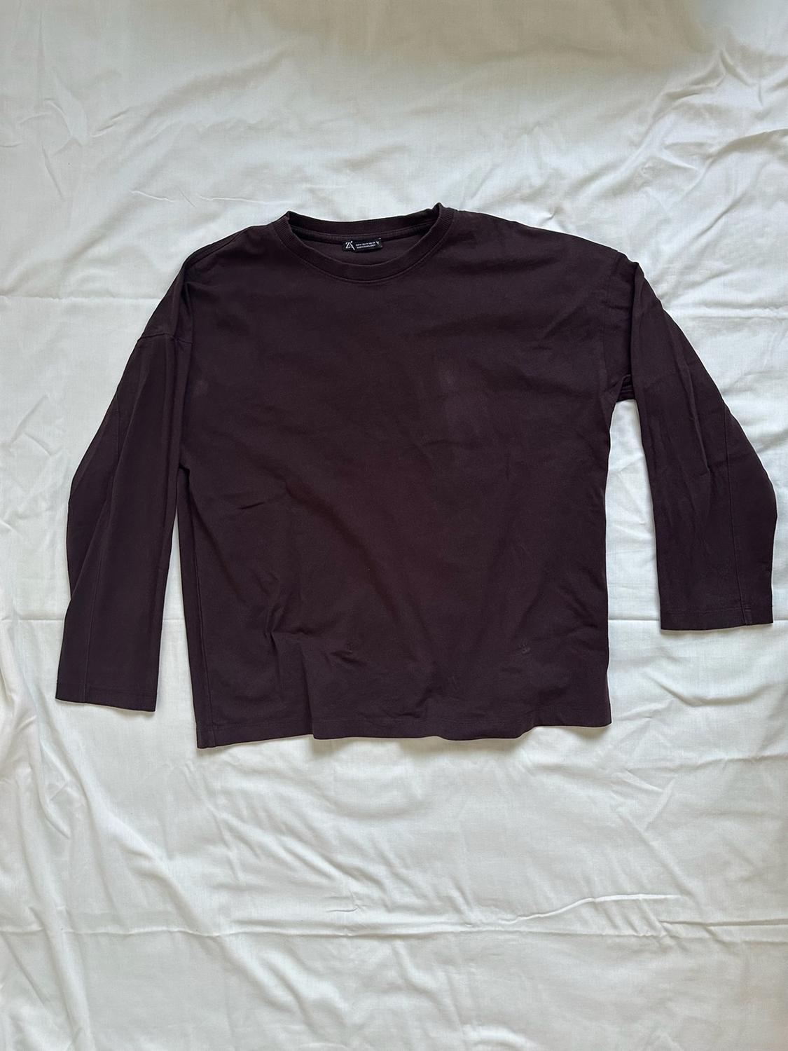 Dark brown long-sleeved t-shirt, laid out on a wrinkled white fabric background that conveys a relaxed style.