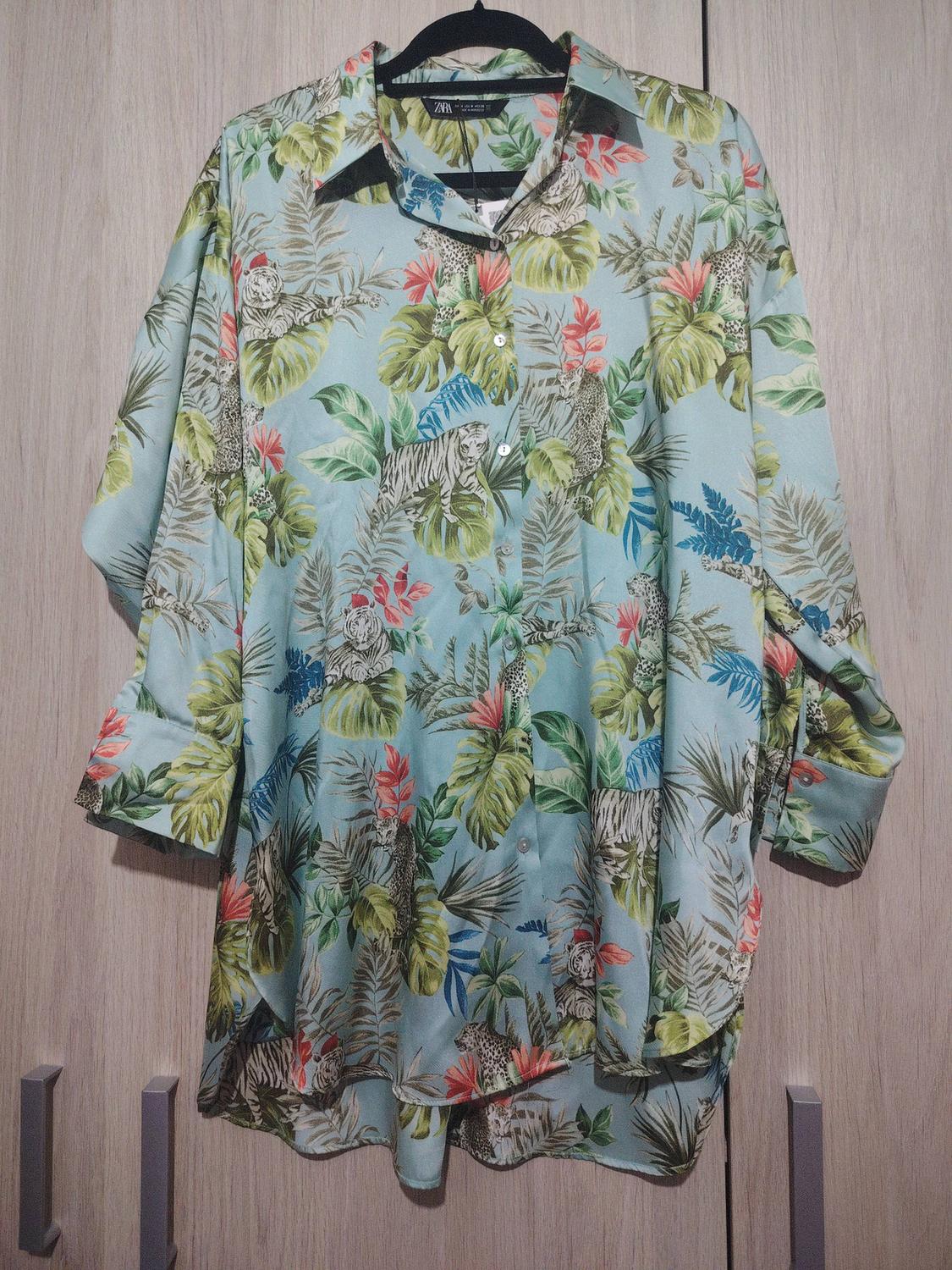 Shirt with a tropical print of green leaves and red flowers on a light blue background, featuring tigers and leopards.