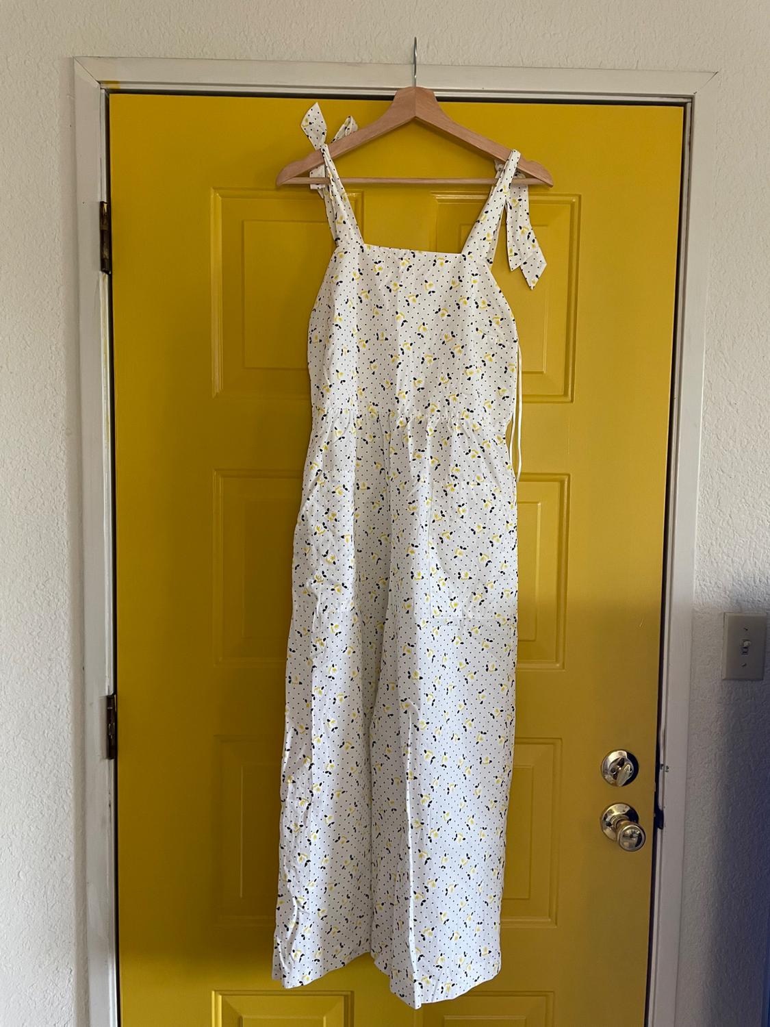 White dress with a black and yellow polka dot print, hanging on a hanger over a yellow door.