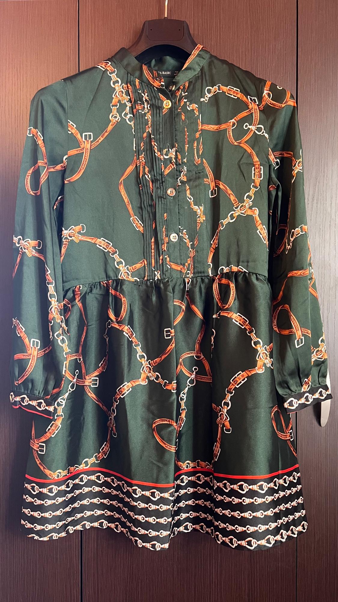 Dark green dress with chain and orange belt print, long sleeves, hanging on a hanger against a wooden background.