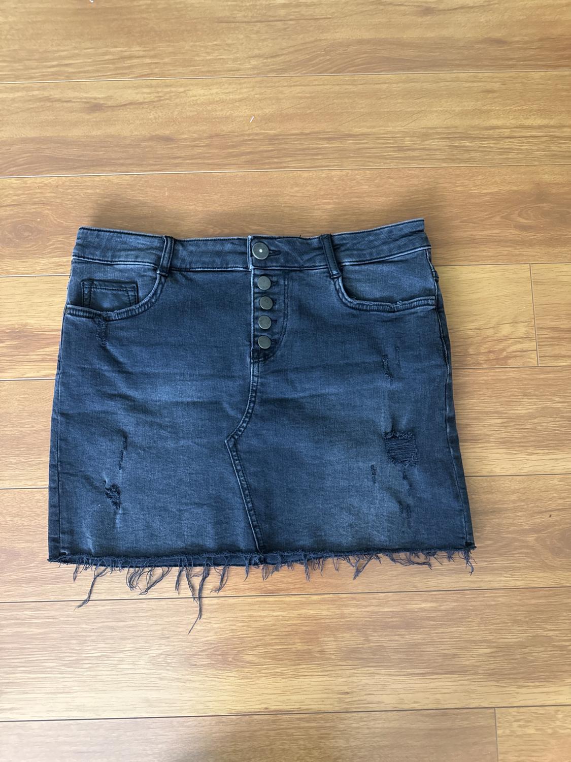 Dark blue denim skirt with front buttons and a frayed hem, on a light wooden floor.
