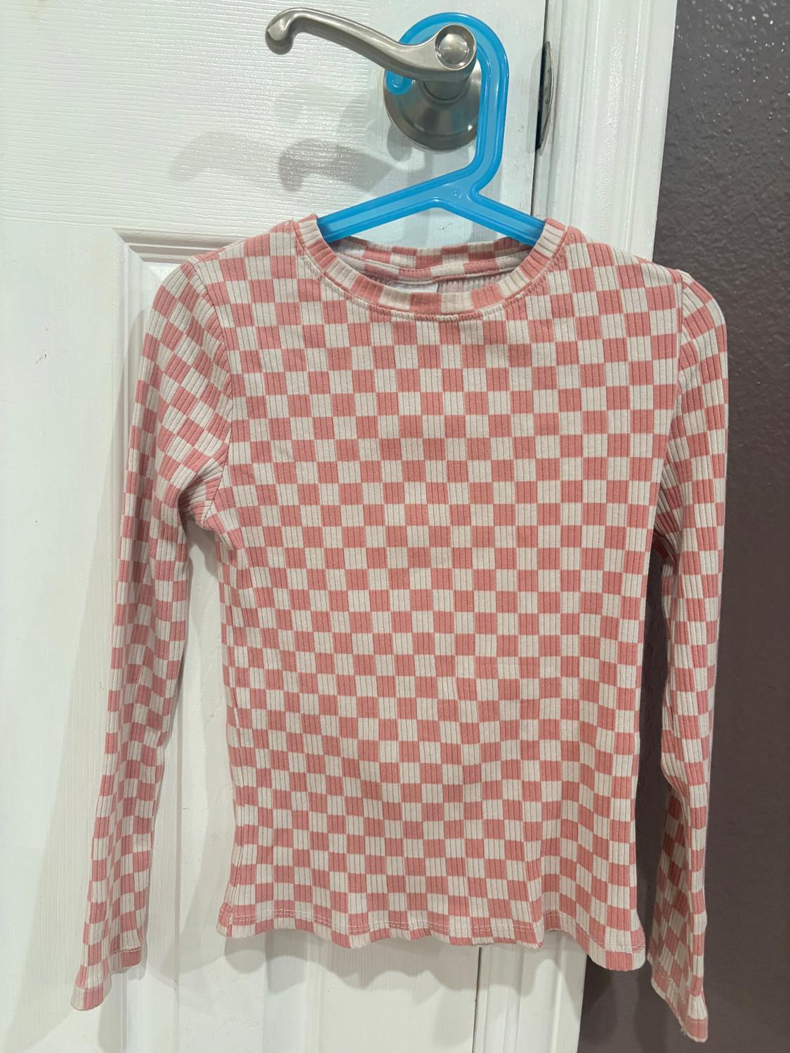Pink and white plaid long-sleeved shirt, hanging on a blue hanger over a white door.