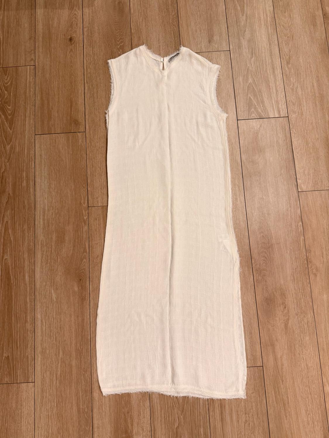 Ecru sleeveless maxi dress with frayed edges, laid out on a wooden floor.