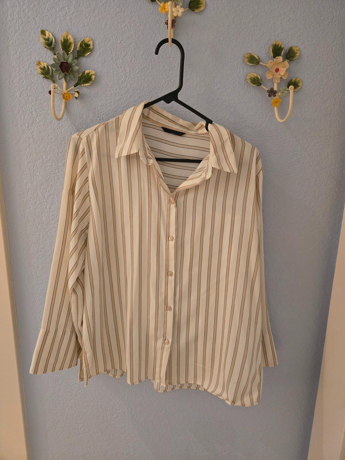 Beige and brown vertically striped shirt hanging on a black hanger against a light blue wall with decorative floral hooks.