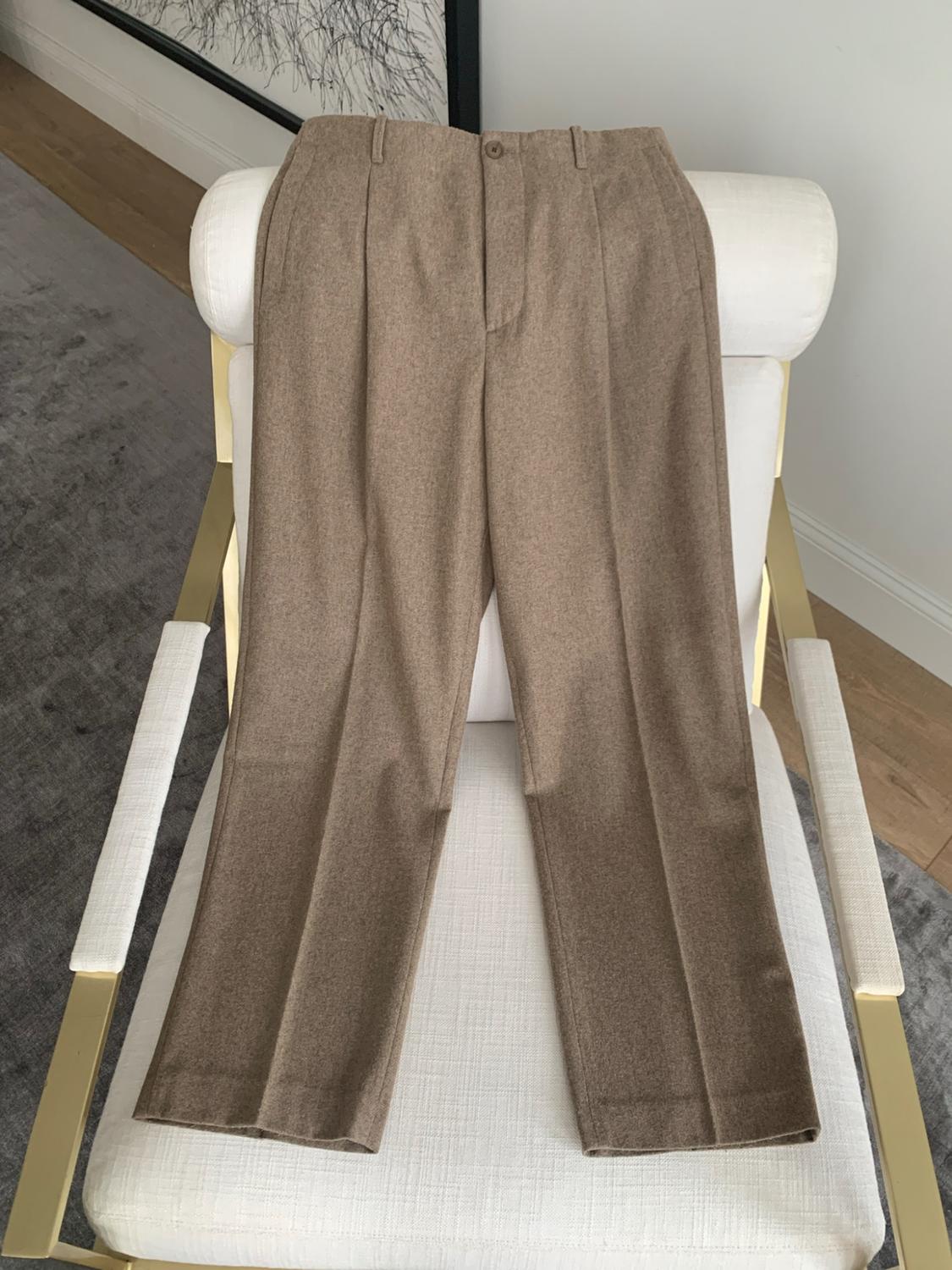 Light brown pleated dress pants, draped over a white chair with a gold frame and a gray rug.