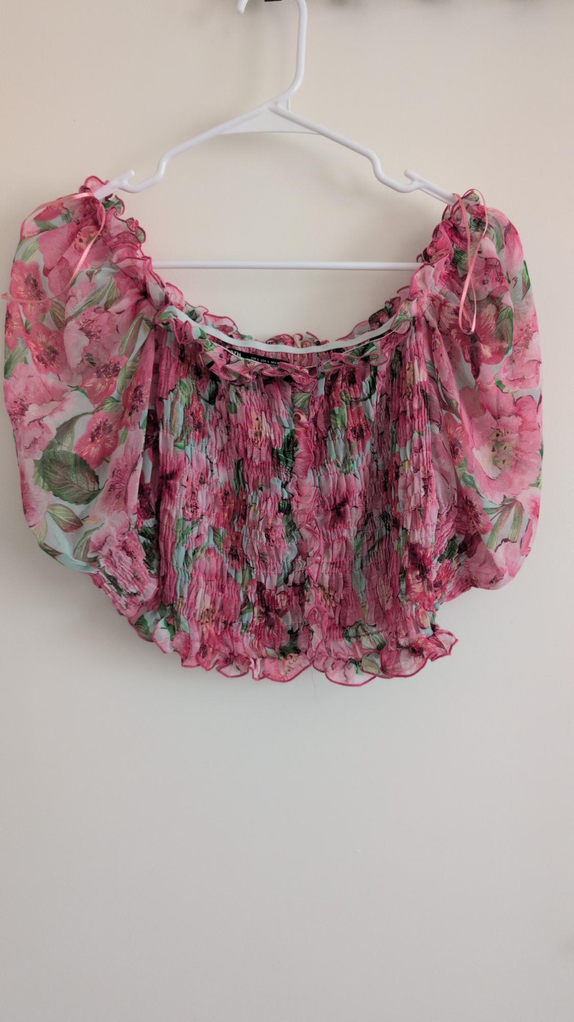 Pink floral print crop top with a smocked bodice and short puff sleeves, hanging on a white hanger against a light background.