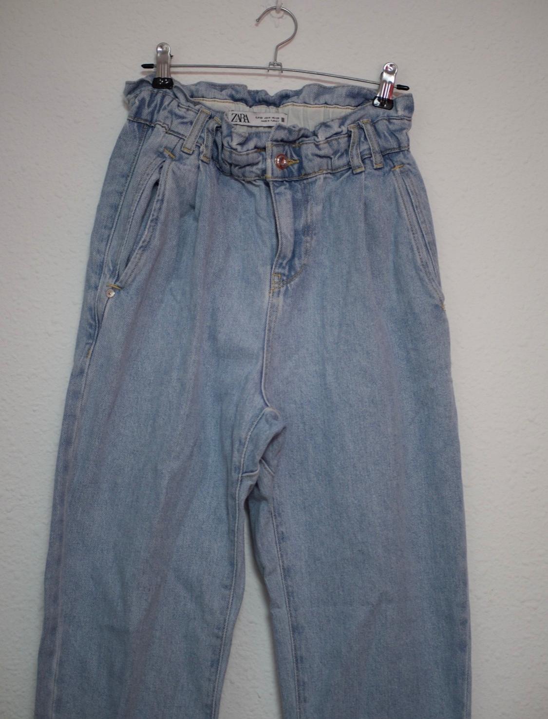 Light blue denim trousers with a gathered waist hanging on a hanger against a white background. Label with the text ZARA.