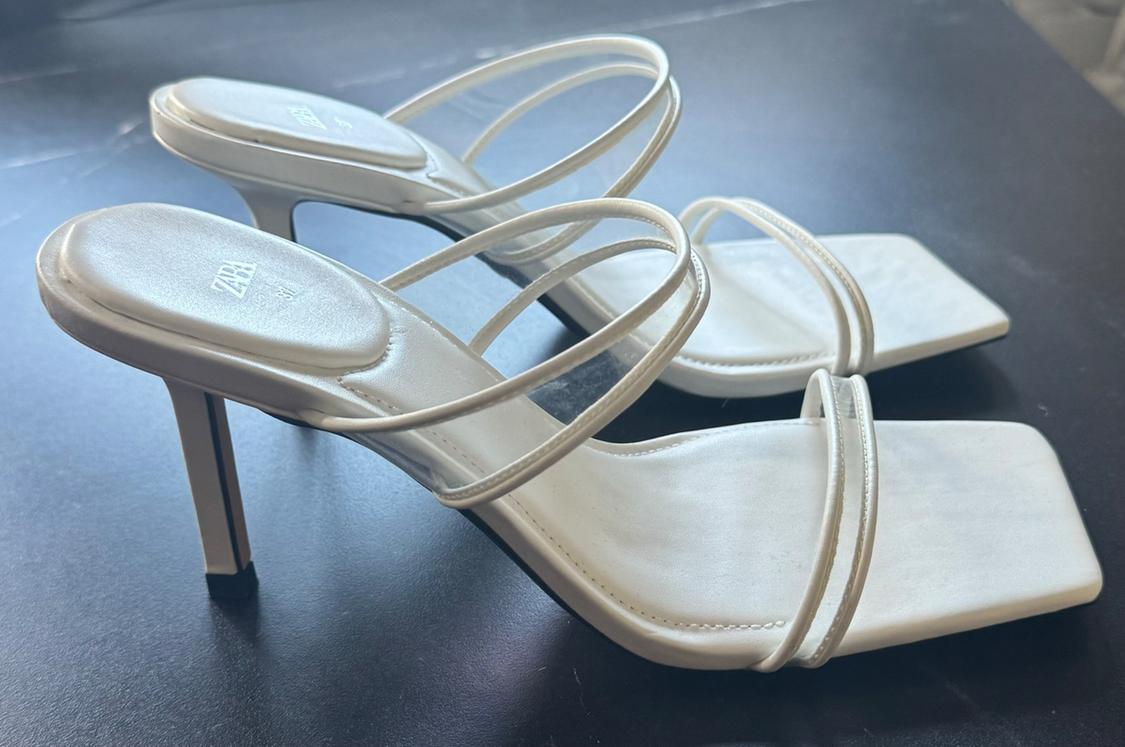 Detail of beige high-heeled sandals with thin straps and a square sole.