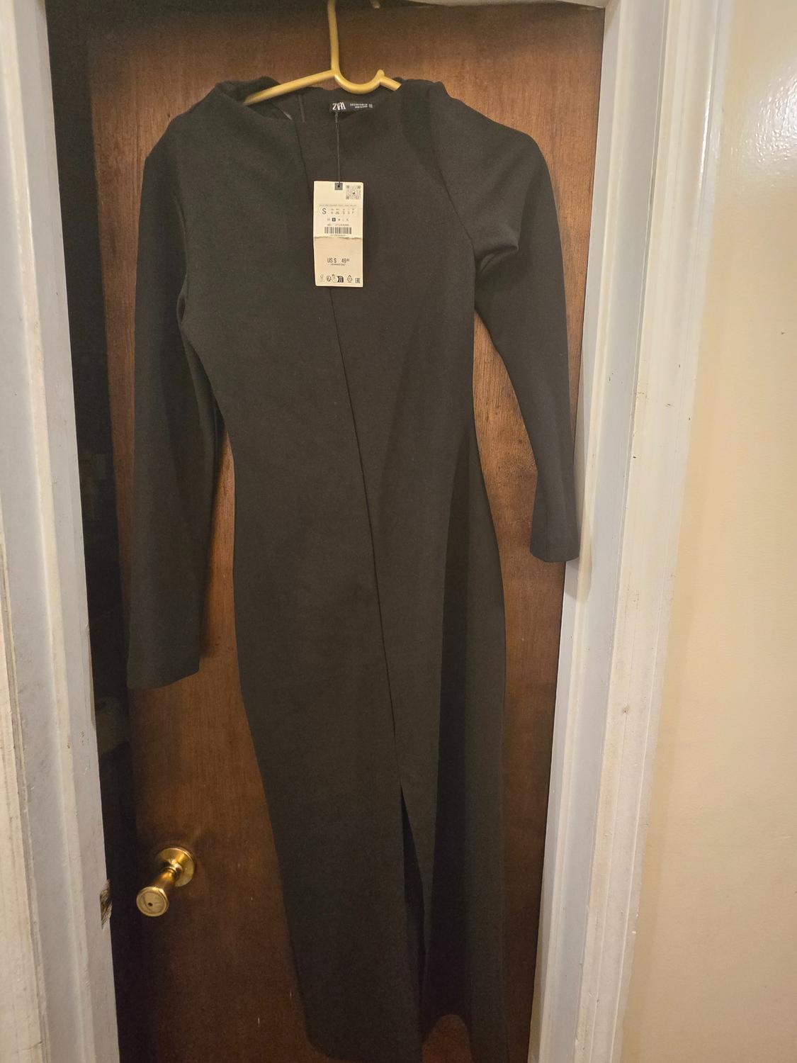 Front view of a black long-sleeved dress with a hanging tag