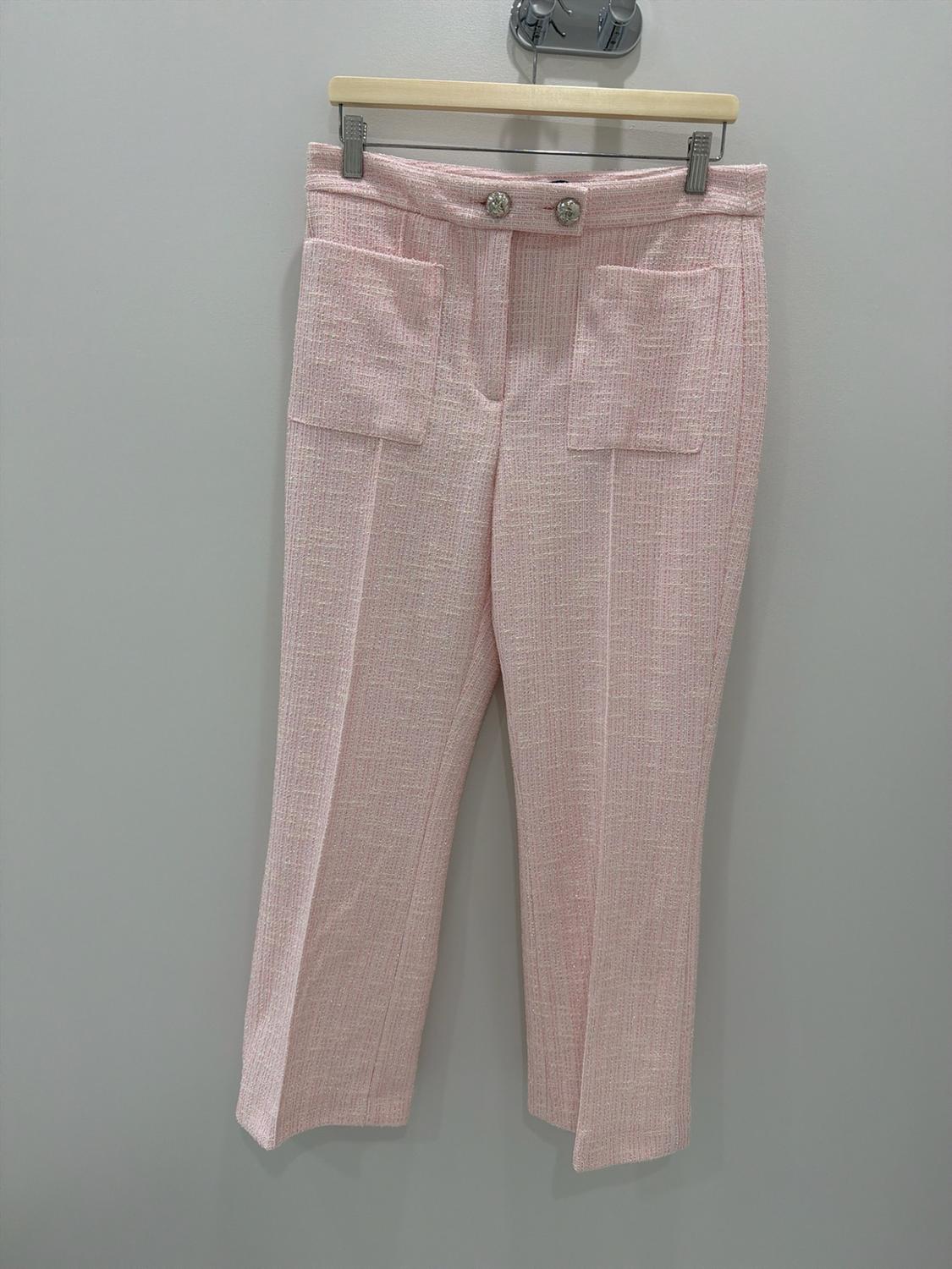 Textured light pink pants hanging on a hanger. They have front patch pockets, a sharp crease, and jeweled buttons at the waist.