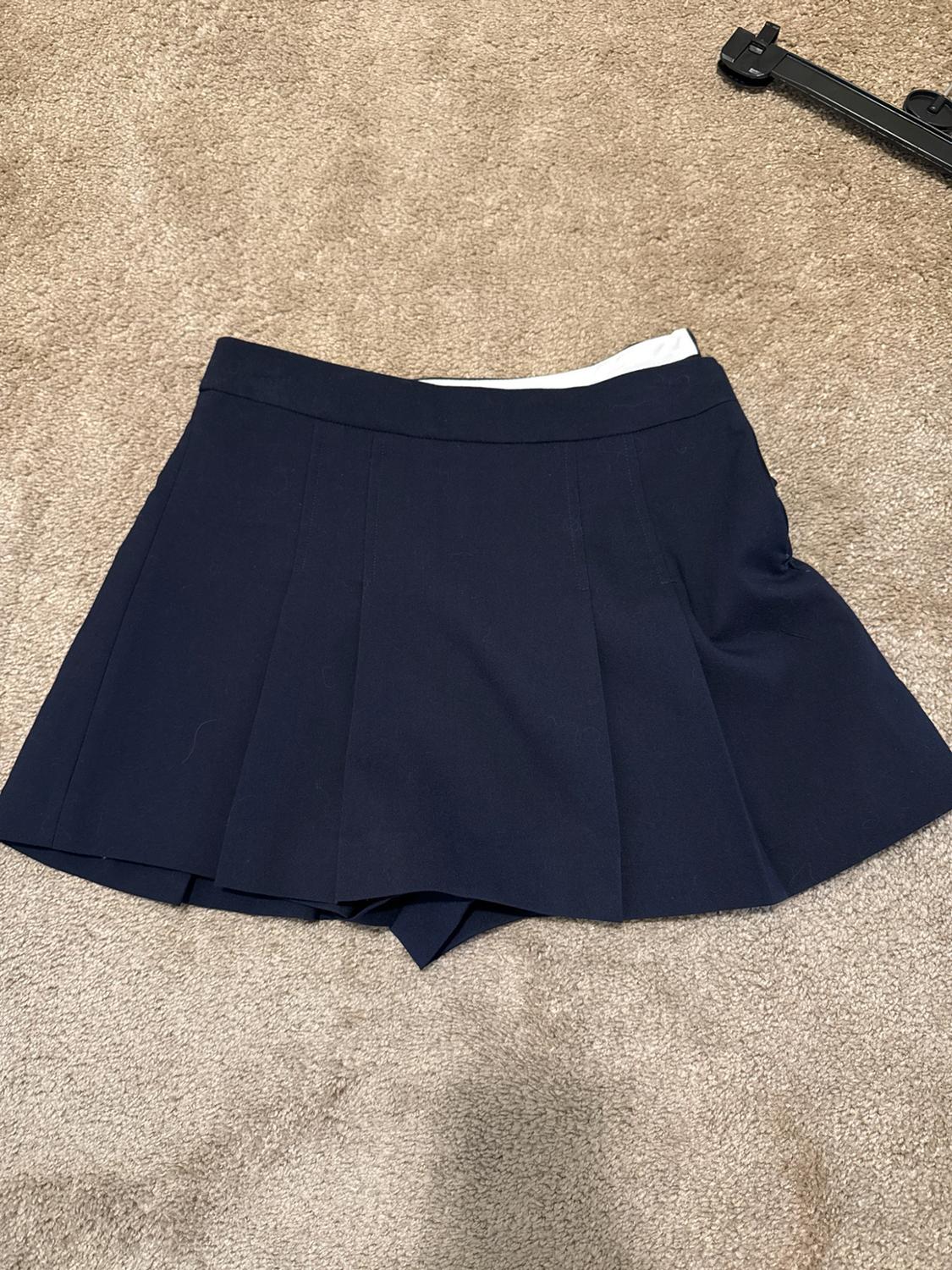 Navy blue pleated skorts on a beige carpet. Black hanger in the top right corner.
