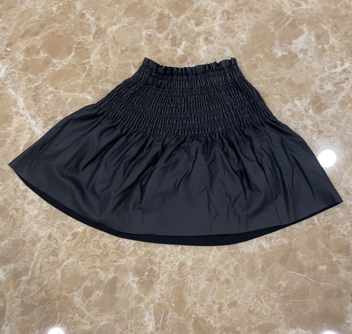 Short black skirt with a wide gathered waist and flared hem, laid out on a beige marble surface.