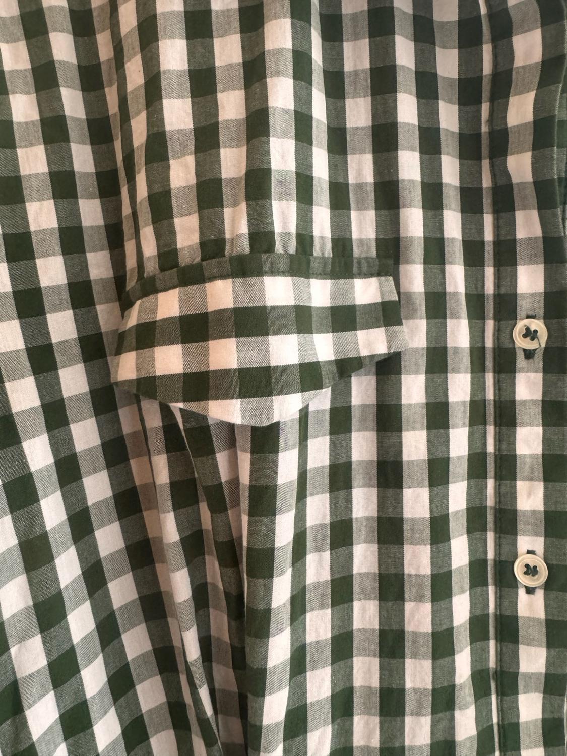 Detail of a green and white checked shirt. The flap of a pocket and two light-coloured buttons are shown on the right-hand side.