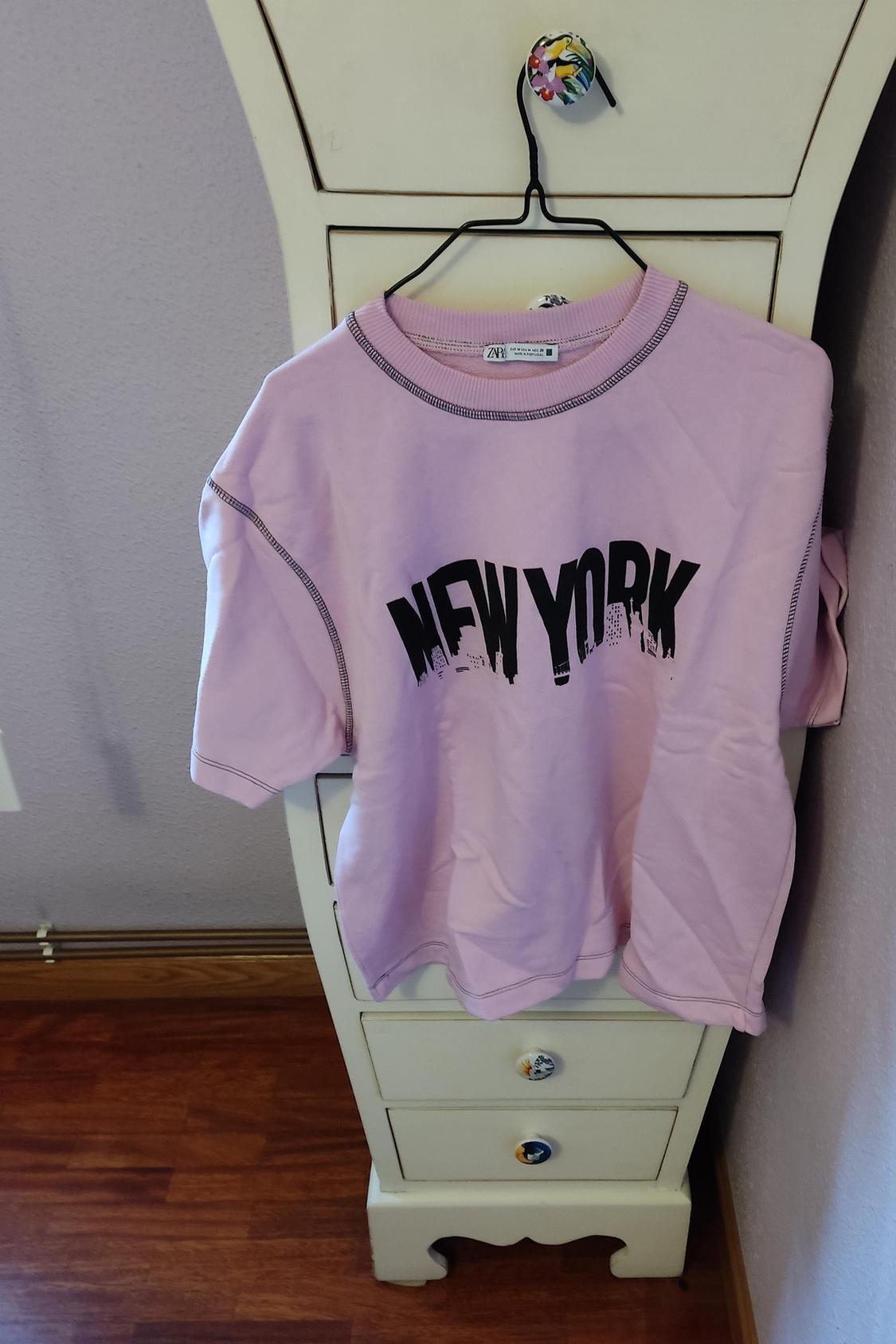 Front view of pink t-shirt with 'NEW YORK' text print in black, visible seams, short sleeve.