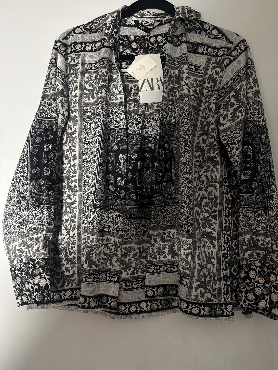 Hanging shirt with black and white floral print, visible label with text "ZARA". White background.