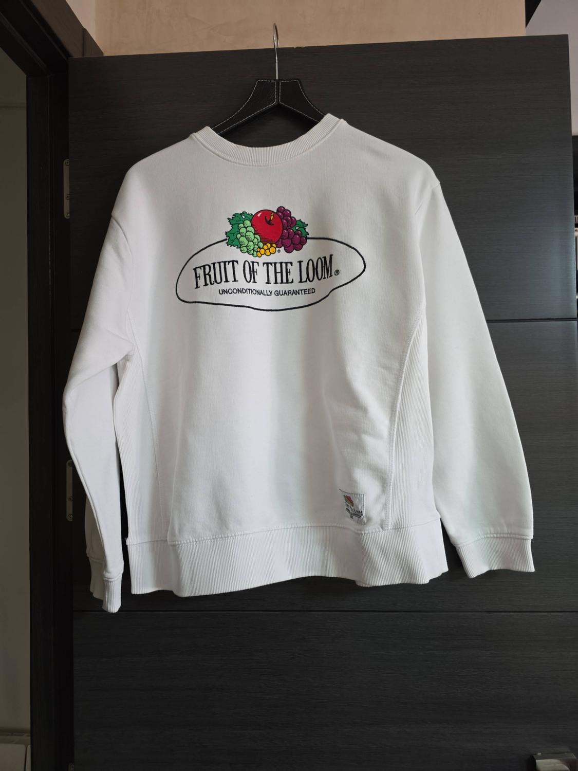 White sweatshirt hanging on a dark door, bearing the text FRUIT OF THE LOOM UNCONDITIONALLY GUARANTEED and a fruit logo.