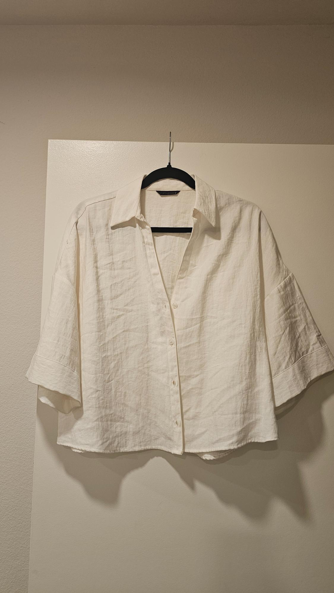 White linen shirt with short sleeves and a classic collar, hanging on a black hanger over a white door.