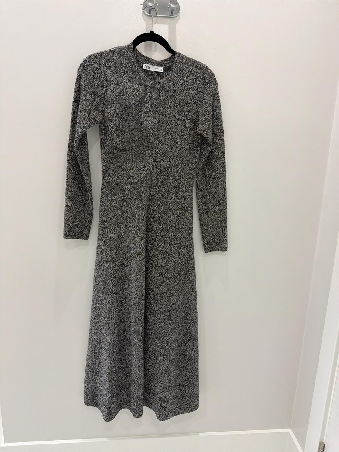Long heather gray knit dress with long sleeves and a round neckline, hanging on a hanger against a white background. ZARA text.